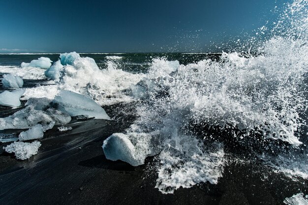 Fale rozbijają się i tworzą snopy piany na blokach lodu odrzuconych na plaży Jokulsarlon