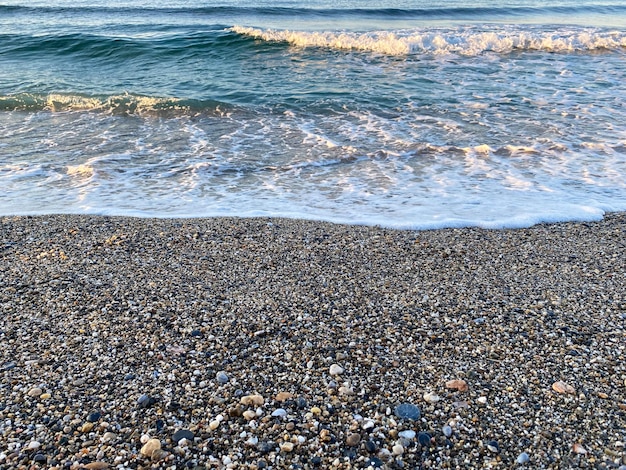 Fale wody w morzu i piasku z małymi naturalnymi wielobarwnymi kamieniami na brzegu morza małe