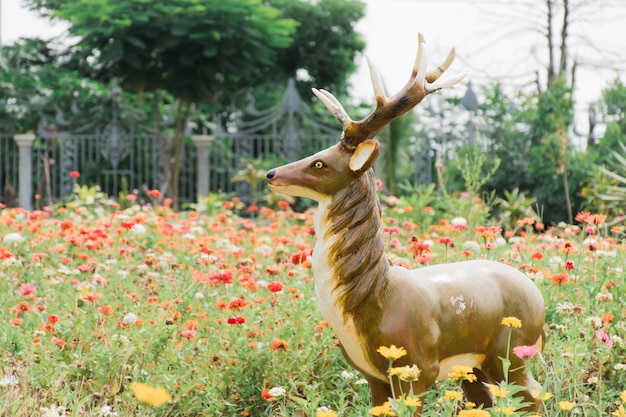 Fałszywy posąg jelenia stoi pośrodku ogrodu kwiatowego.
