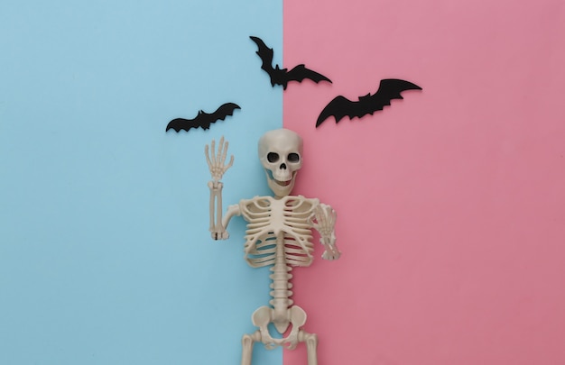 Fałszywy szkielet i nietoperze na różowym niebieskim pastelu. Halloweenowa dekoracja, przerażający motyw