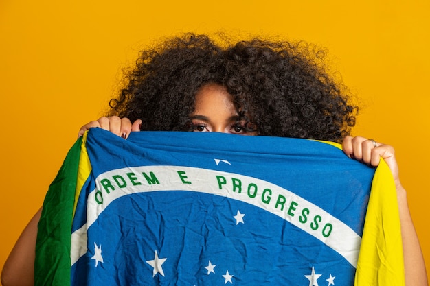 Zdjęcie fan tajemniczej kobiety z czarną flagą na twarzy. kolory brazylii w ścianie, zielony, niebieski i żółty. wybory, piłka nożna lub polityka.