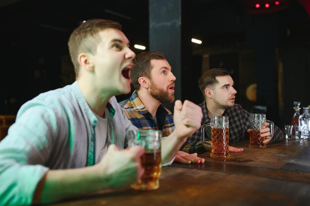 Fani piłki nożnej w barze Szczęśliwi kibice piłki nożnej wiwatują w barze i piją piwo, podczas gdy barman serwuje piwo w tle