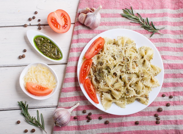 Farfalle Makaron Z Sosem Pesto, Pomidorami I Serem Na Lnianym Obrusie Na Białym Tle Drewnianych.