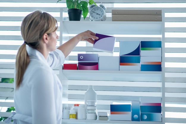 Zdjęcie farmaceuta w fartuchu laboratoryjnym kładzie lekarstwo na półce