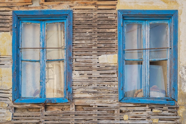 Fasada rozpadającego się starego drewnianego domu z niebieskimi oknami Opuszczone domy starego pomysłu miasta na tło