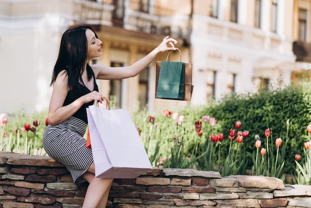 Fashionably ubrana kobieta z kolorowych torby na zakupy siedzi w pobliżu kwiaty na ulicach, koncepcja zakupów