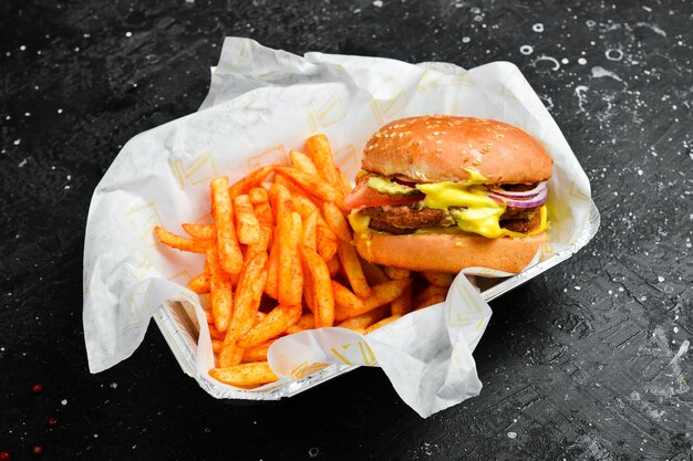 Zdjęcie fast food frytki i hamburger w jednorazowym naczyniu na drewnianej desce