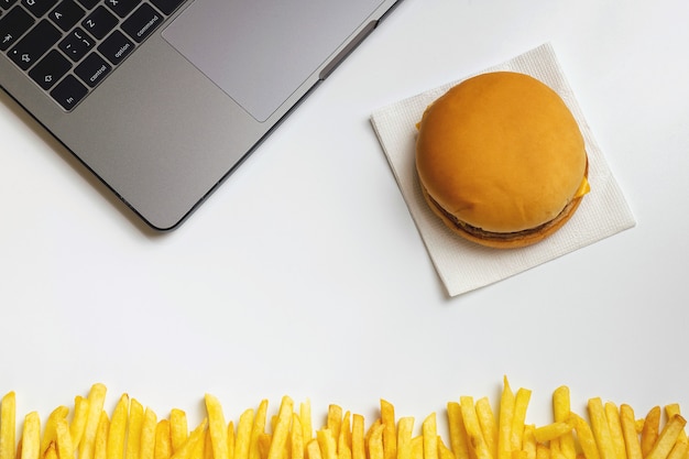 Fast food w pracy przekąski. Laptop, hamburger i francuski smażyć w miejscu pracy.