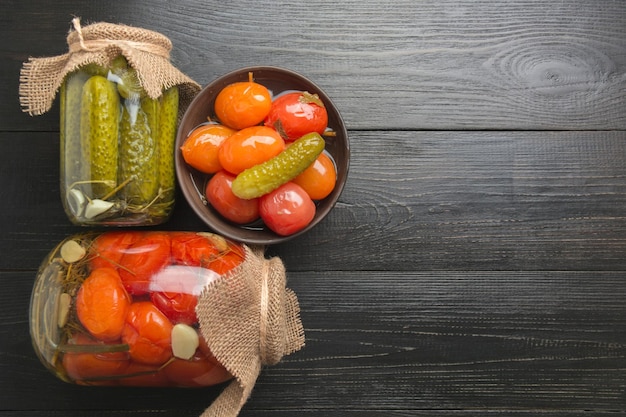 Fermentowane warzywa w puszkach ogórek i pomidor w szklanych słoikach na czarnej drewnianej desce Widok z góry Mieszkanie w stylu świeckim Domowe preparaty do zbiorów i jesieni Miejsce na tekst