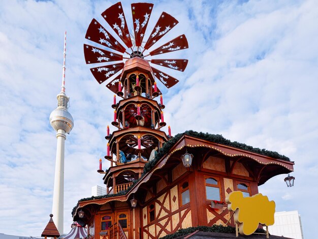 Fernsehturm i karuzela bożonarodzeniowa na jarmarku bożonarodzeniowym na Alexanderplatz w Berlinie, zimowe Niemcy. Dekoracje na jarmark adwentowy i stragany z artykułami rzemieślniczymi na bazarze.