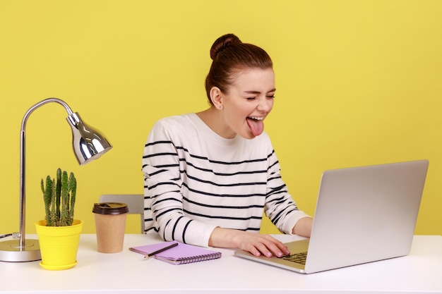 Figlarna pracownica biurowa w pasiastej koszuli pokazująca język wyrażający pozytywne dziecinne emocje