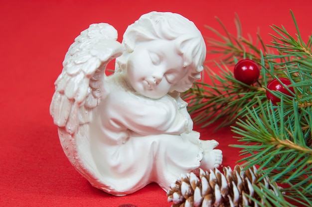 Zdjęcie figurka anioła bożego narodzenia siedzącego w pobliżu gałęzi choinki z szyszkami na czerwonym tle