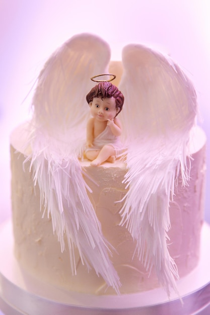 Figurka aniołka ze skrzydłami siedzi na białym torcie Zbliżenie