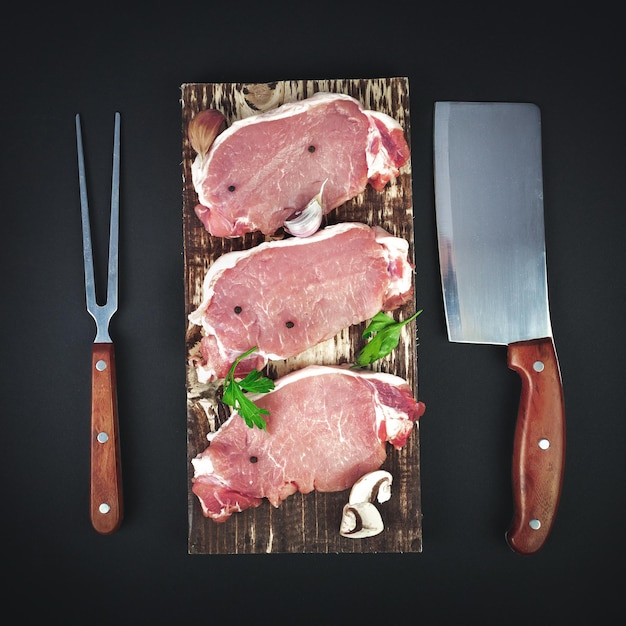 Filet stek wołowy na desce do krojenia w kuchni ze składnikami do gotowania noża i widelca do mięsa na ciemnym tle