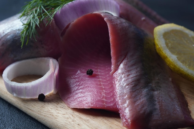 Filet z ryby śledziowej na desce z pieprzem, ziołami, czerwoną cebulą i cytryną