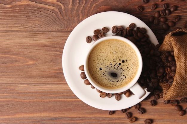 Filiżanka aromatycznej kawy i ziaren kawy na drewnianym tle