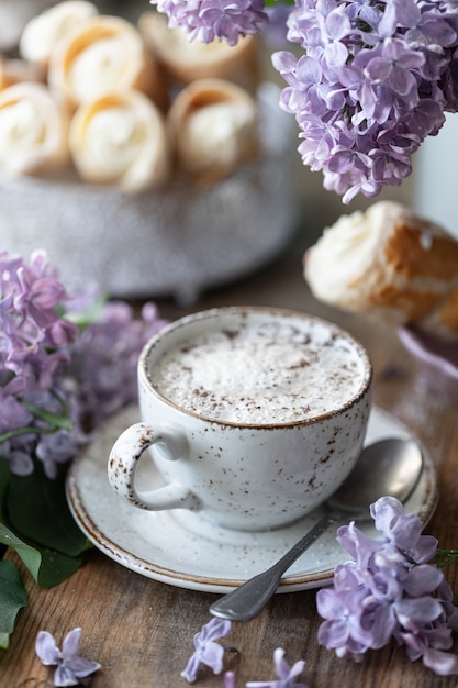 Filiżanka Cappuccino I Rożków Z Ciasta Francuskiego Z Kremem Waniliowym W Metalowym Pudełku Na Wiosnę Martwa Natura Z Bukietem Bzu Na Drewnianym Stole