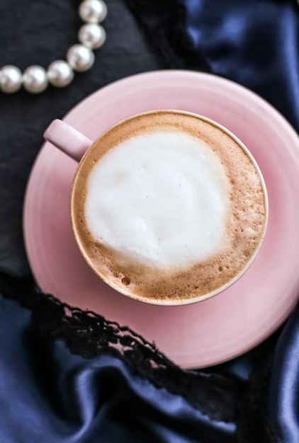 Filiżanka cappuccino na śniadanie z satynową i perłową biżuterią w tle organiczna kawa z mlekiem bez laktozy w paryskiej kawiarni dla luksusowej marki wakacyjnej w stylu vintage