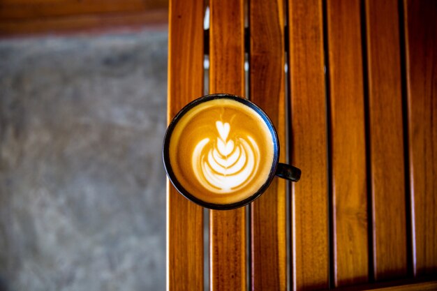 Filiżanka cappuccino z latte art na drewnianym tle. Piękna pianka, drewniane biurko i cegła ściana.