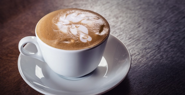 Filiżanka capuccino z bogatą dekoracyjną pianką na wierzchu na ciemnym drewnianym stole.