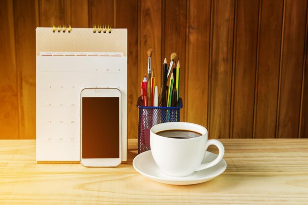 Zdjęcie filiżanka do kawy i smartfon z kalendarzem na drewnianym stole