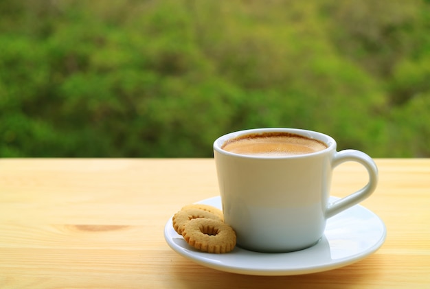 Filiżanka gorącej kawy i ciasteczka na drewnianym stole na zewnątrz z rozmytym zielonym liściem