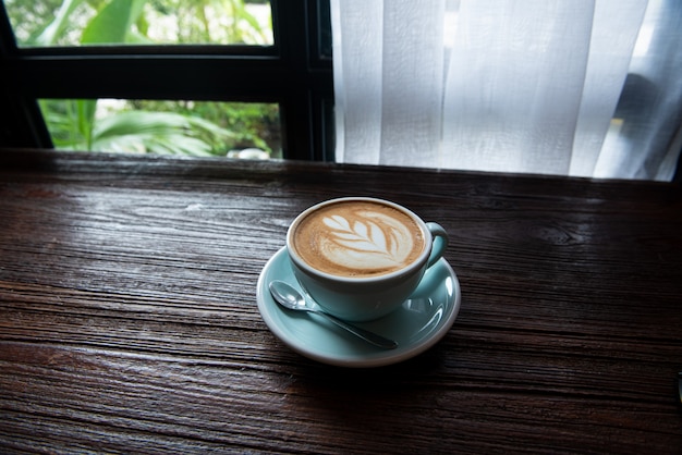 Filiżanka gorącej kawy Latte na drewnianym stole przy oknie