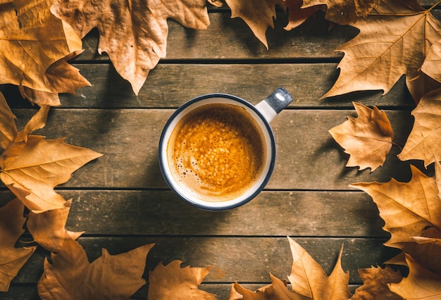 Filiżanka gorącej kawy na starym drewnianym stole z jesiennymi liśćmi Domowa atmosfera i relaks