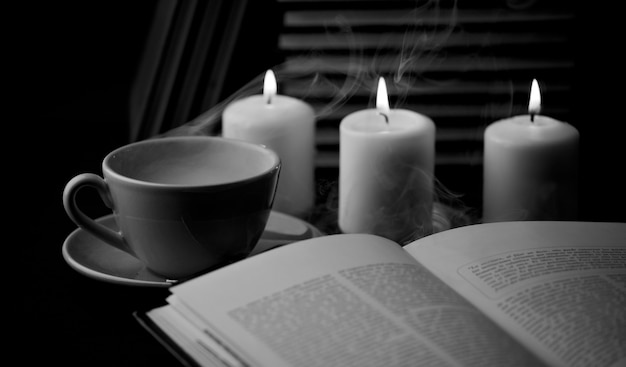 filiżanka gorącej kawy z książką i świecami w czarno-białym tle