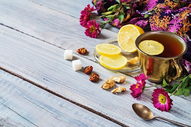 Filiżanka herbaty, cytryny i kwiatów na białym drewnianym stole