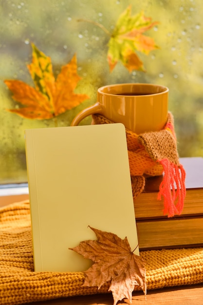 Filiżanka herbaty, jesienne liście, książki, notatnik i czerwona dzianinowa krata na drewnianym stole