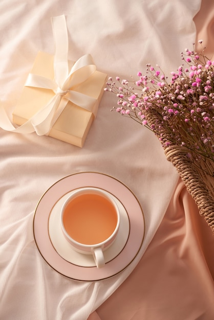 Filiżanka herbaty, pudełko upominkowe i kwiaty na jasnym tle