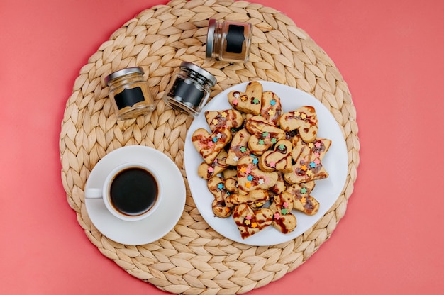 Zdjęcie filiżanka kawy, domowe ciasteczka i naczynia kuchenne na różowym tle.