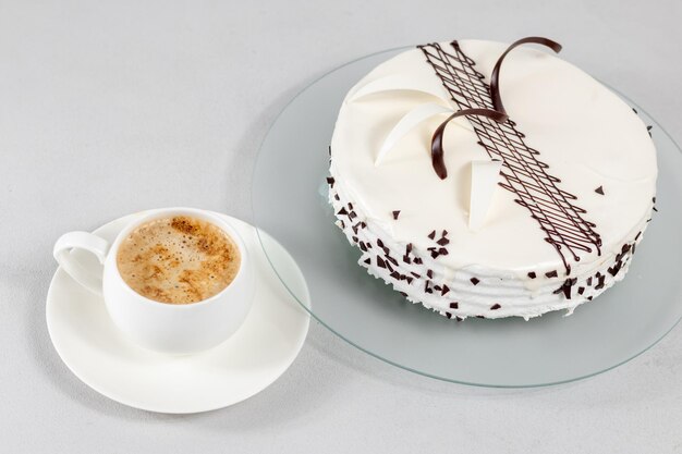 Filiżanka kawy i biały tort ozdobiony dekoracją czekoladową na szklanym talerzu na szarym tle Selektywna ostrość