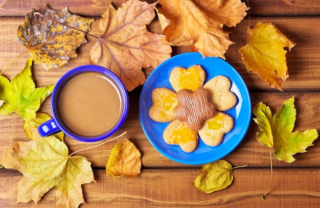 Filiżanka kawy i ciasteczka na stole z suszonymi jesiennymi liśćmi. Picie kawy jesienią na drewnianym stole otoczonym suchymi liśćmi jesieni