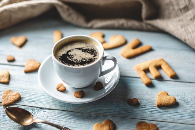Filiżanka kawy i wiadomość od słodkiego ciasteczka w formie słowa miłość na niebieskim tle drewnianych