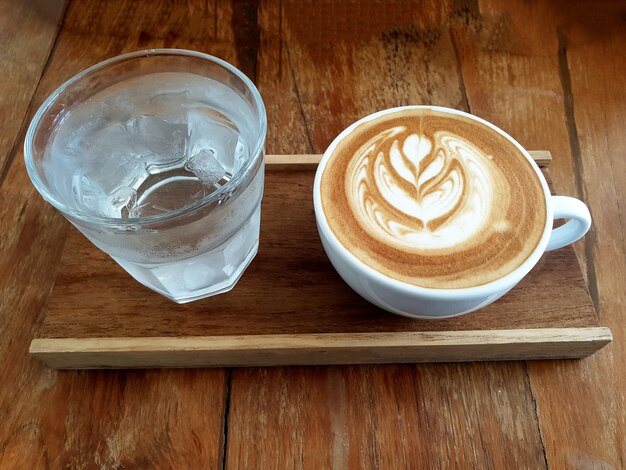 Filiżanka kawy latte art z wodą pitną na drewnianym tle