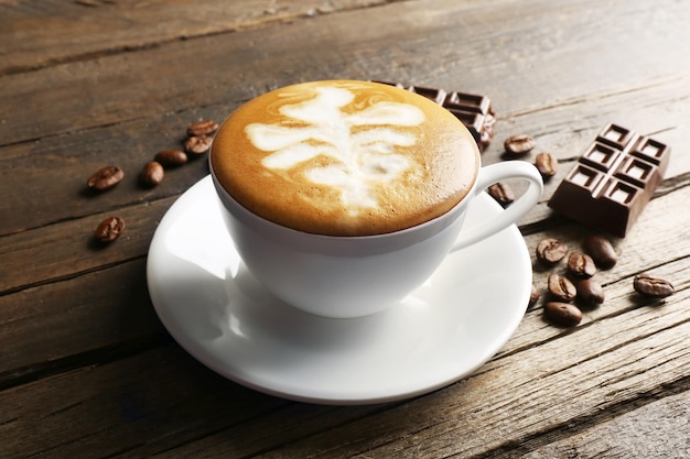 Zdjęcie filiżanka kawy latte art z ziarnami i czekoladą na drewnianym tle