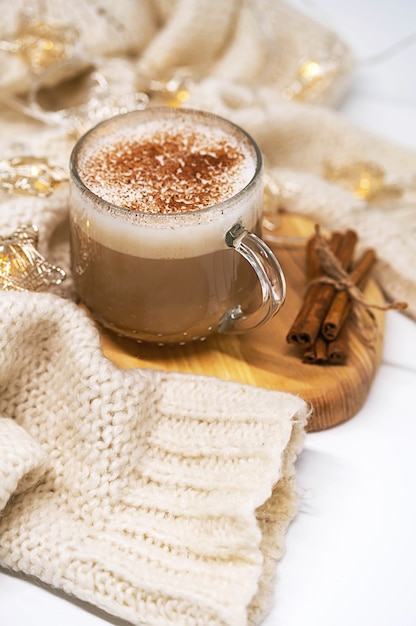 filiżanka kawy latte z cynamonowym białym swetrem i bożonarodzeniowymi girlandami