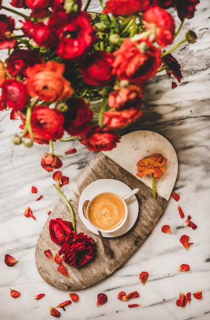 Zdjęcie filiżanka kawy na desce do serwowania i czerwone kwiaty ranunculus