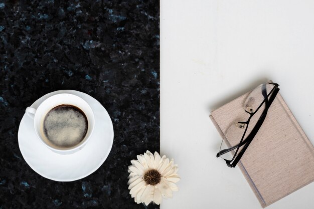 Zdjęcie filiżanka kawy, notatnik, szklanki w czarnych ramkach i kwiatek na czarno-białym tle