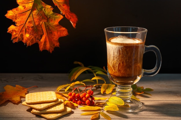 Filiżanka kawy z mlekiem obok jesiennych liści jarzębiny i ciasteczek