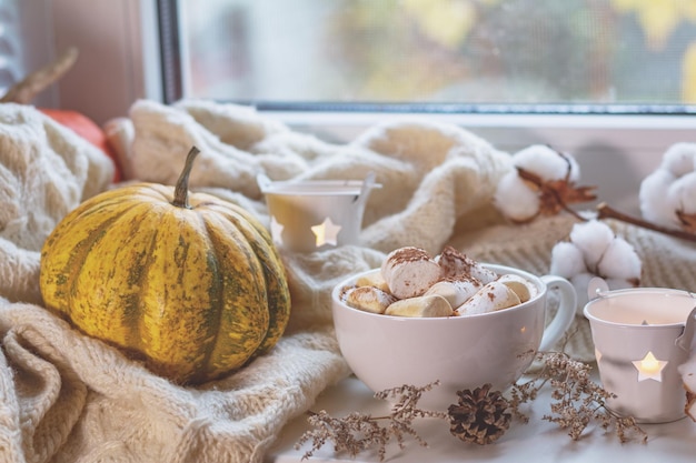 Zdjęcie filiżanka kawy z pianką na parapecie koncepcja przytulnego domu piękne kartki świąteczne świece bawełniane gałęzie kwiatowe i biała wełna dziewiarska