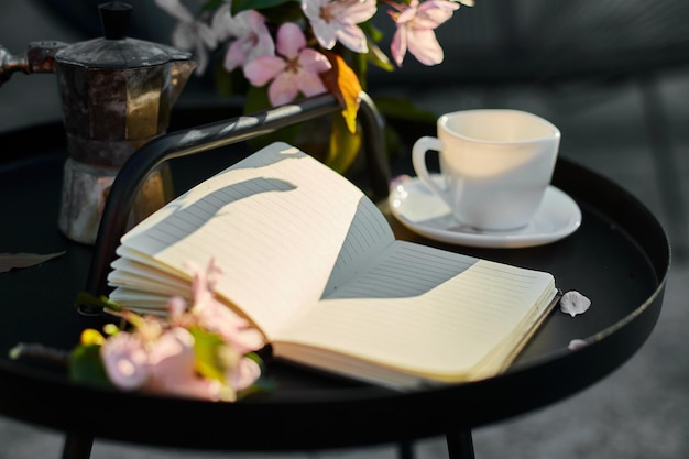 Filiżanka kwiatów kawy i notatnik na małym czarnym stole
