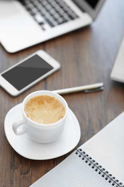 Filiżanka świeżej kawy obok smartfona i laptopa na stole biurowym