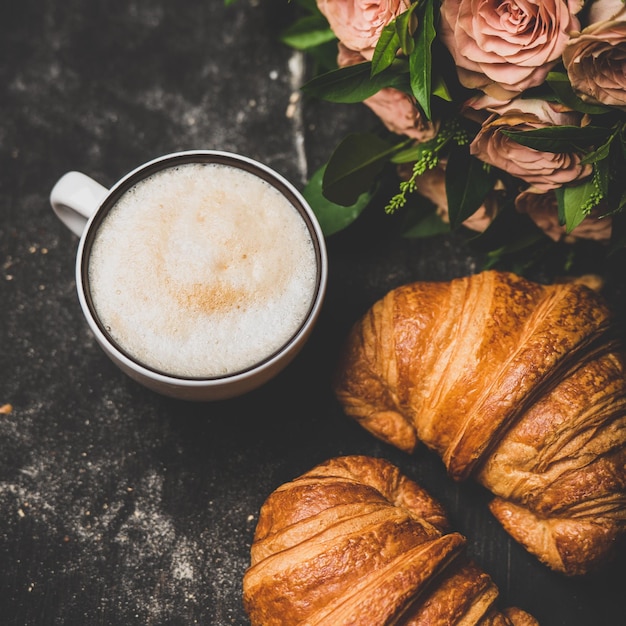 Filiżanka świeżych rogalików cappuccino i kwadratowe różowe kwiaty