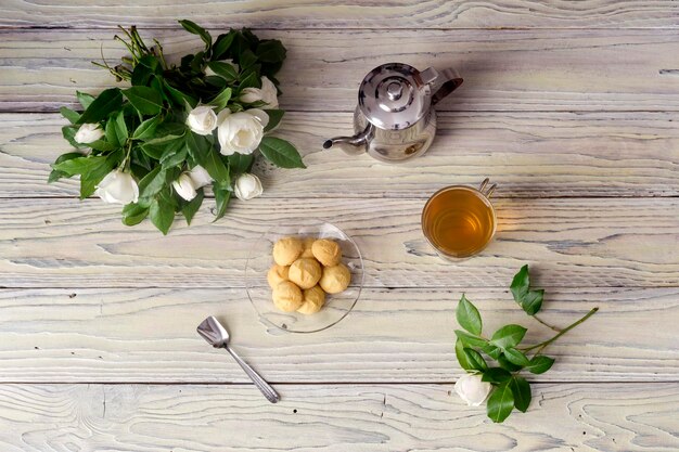 Filiżanka z bukietem herbaty z białych róż i kruche ciastko na drewnianym stole zbliżenie