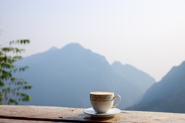 Filiżankę gorącej kawy umieszcza się na drewnianym tarasie na tle góry