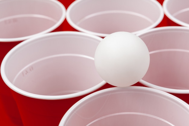 Zdjęcie filiżanki i plastikowa piłka na czerwieni powierzchni. gra pong piwny
