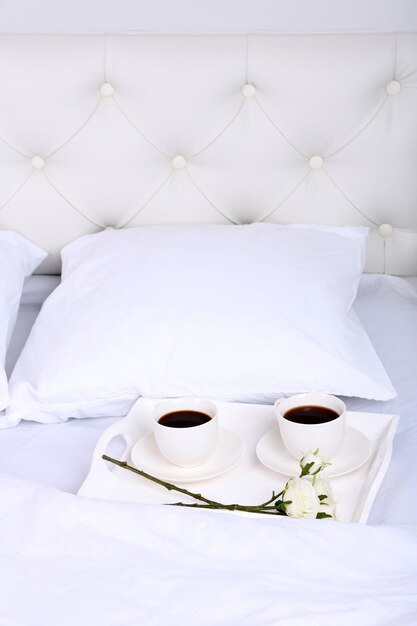Filiżanki kawy na wygodnym miękkim łóżku z poduszkami